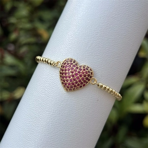 Detalle de pulsera de cuentas doradas con colgante de corazón en circonita rosa