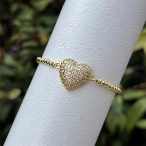 Primer plano de pulsera dorada con dije de corazón y circonitas en un pedestal blanco