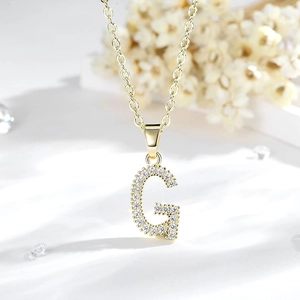 Dettaglio macro del ciondolo lettera G placcato oro 14K con pietre di zircone su catena