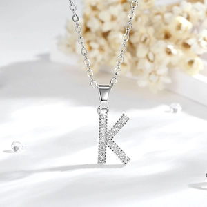 Dettaglio macro di un ciondolo a lettera K in argento con zirconi su una catena chic