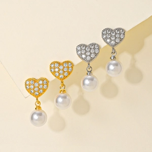 Elegant gold and silver heart earrings with pavé zirconia and pearl drops on beige background
