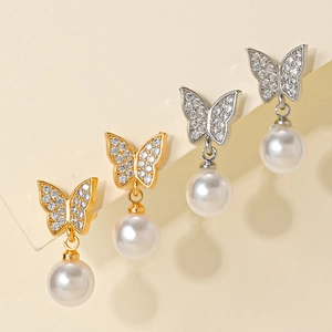 Close-up of gold and silver butterfly pearl earrings with sparkling zircon inlay