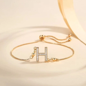 Close-up of a gold-plated adjustable bracelet with a zircon-encrusted letter H pendant