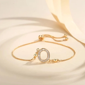 Detail of gold adjustable bracelet with sparkling letter O charm and sliding buckle clasp
