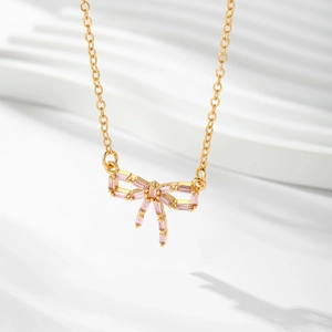 Vue détaillée du collier nœud doré avec cristaux baguette roses et pampilles élégantes
