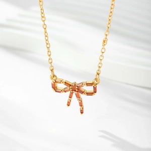 Vue détaillée du pendentif nœud plaqué or avec zircons ambrés sur fond texturé blanc