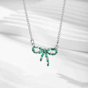 Gros plan d'un pendentif nœud argenté avec zircon vert sur une chaîne à maillons fins