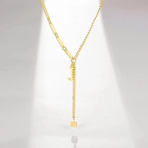 Detail of gold Y-shaped necklace featuring a letter J pendant and tassel cubic charm