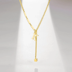 Detail of gold letter K tassel pendant on Y-shaped necklace with polished metal bar links