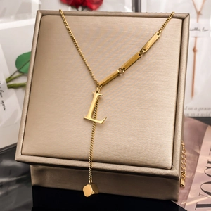 Detail of gold letter L pendant necklace with rectangle bar chain and tassel cubic charm