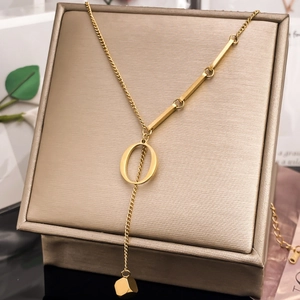 Detail of gold letter O necklace with geometric bars and cube pendant on leather stand