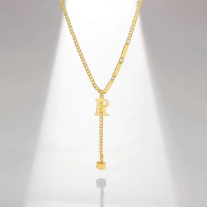 Detail of gold letter R pendant necklace with asymmetric chain and cube tassel