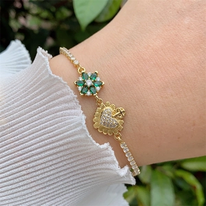 Detailed close-up of a gold-plated bracelet with zircon flower and heart charms on a wrist