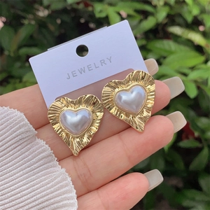 Dettaglio di orecchini a cuore in oro 18K con bordi plissettati e perla bianca
