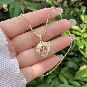 Detail of 18K gold heart pendant with crystal letter I held against nature background