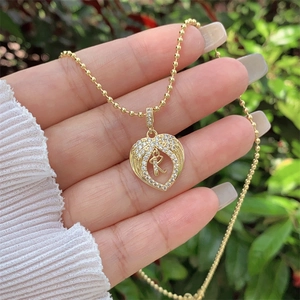 Macro detail of 18K gold plated heart wing pendant with zircon letter R on beaded chain