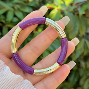 Detail of purple and gold beaded stretch bracelet on wrist with outdoor background