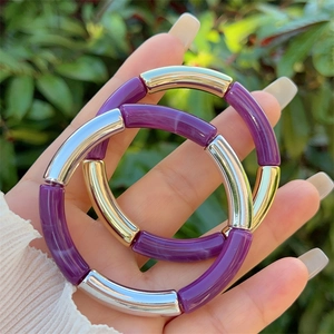 Close-up of purple resin and metallic bamboo tube bangles held in hand outdoors