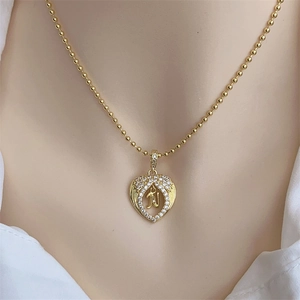 Close-up of 18K gold plated heart necklace with zircon paved letter J on white collar