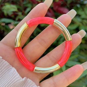 Detail of neon pink resin and gold curved tube stretch bracelet on a female wrist