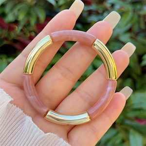 Detail view of pink marble resin and golden metal tube bracelet worn on hand