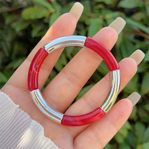 Modern resin bracelet with red and silver curved tubes held in hand against green leaves