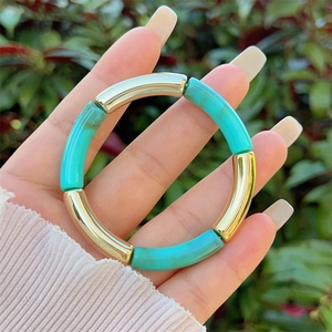 Detail of turquoise resin and gold metal curved tube beaded bracelet on a person hand