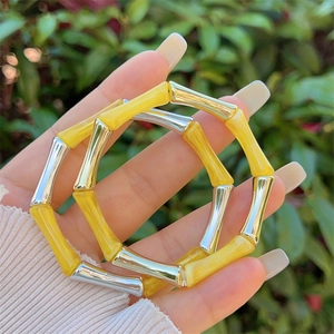 Dettaglio dei braccialetti in resina gialla stile bambù indossati sulla mano all'aperto
