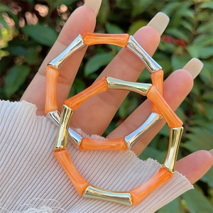 Dettaglio di braccialetti in resina marmorizzata arancione e metallo in stile bamboo