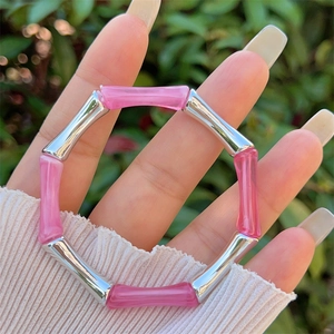 Bracciale in resina a bambù rosa e argento tenuto in mano con sfondo naturale esterno