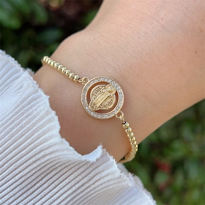 Close-up of golden beaded bracelet with San Benito medal and sparkling zircon frame
