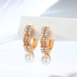 Macro detail of gold-plated hoop earrings with pavé zircon stones and a hanging white pearl