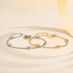 Detalle de pulseras de bolas en plata y oro con cierre de mosquetón y colgante de corazón