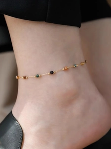Detalle de una tobillera de acero inoxidable dorado con piedras naturales de colores