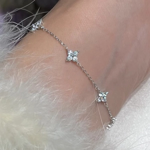 Elegante cavigliera a quadrifoglio argento con zirconi bianchi su sfondo morbido di peluche