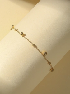 Detaillierte Nahaufnahme der goldenen Perlen-Fußkette mit polierten Metallkugeln auf Beige