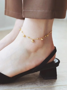 Detail eines goldenen Fußkettchens mit Perlen, getragen mit Sandalen im Strand-Stil