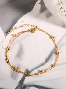 Detail eines goldenen zweilagigen Perlen-Fußkettchens mit Karabinerverschluss auf Stoff