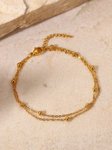 Detailaufnahme des goldenen zweilagigen Perlen-Fußkettchens auf Stein-Hintergrund