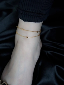 Nahaufnahme einer zweilagigen goldenen Fußkette mit kleinen Perlen auf dunklem Satin