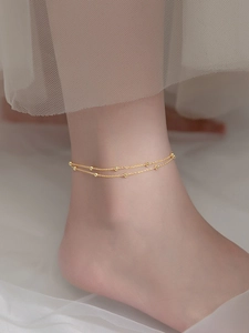 Detailaufnahme einer goldfarbenen Fußkette mit kleinen Perlen am Knöchel des Models
