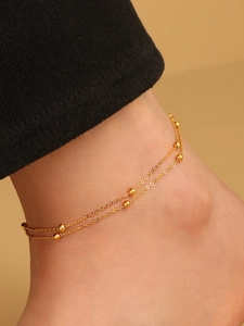 Nahaufnahme eines doppellagigen goldenen Fußkettchens mit Perlen im minimalistischen Design