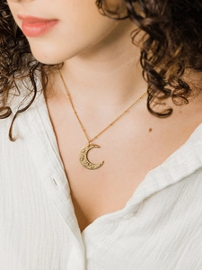 Detail van gouden halve maan hanger met fijne gravures aan een verfijnde kralenketting