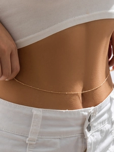 Close-up of a minimalist gold beaded waist chain jewelry worn on a female model