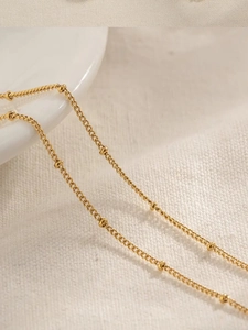 Detail of a minimalist gold beaded waist chain resting on a premium textured cloth