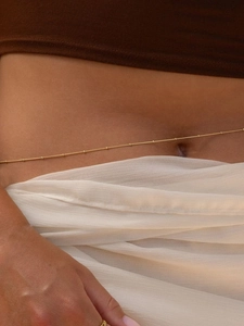Detail of a thin gold beaded waist chain showing elegant bohemian style on a model waist