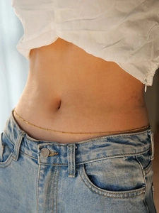 Detailed view of a gold beaded waist chain accessory on a model with blue jeans