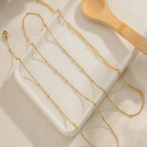 Golden beaded waist chain with lobster clasp on white ceramic tray with linen fabric background