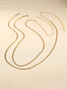 Detail of two golden flat snake bone waist chains with lobster clasps and adjusters