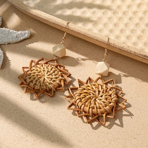 Bohemian handmade straw woven earrings with wooden beads on beach sand background